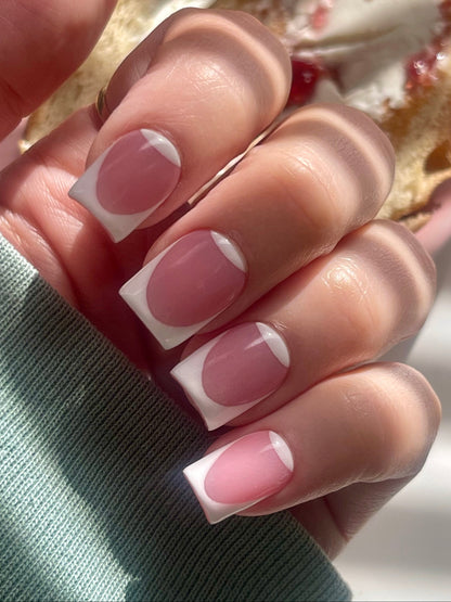 Close-up of a hand with pink and white nail polish holding a pastry.