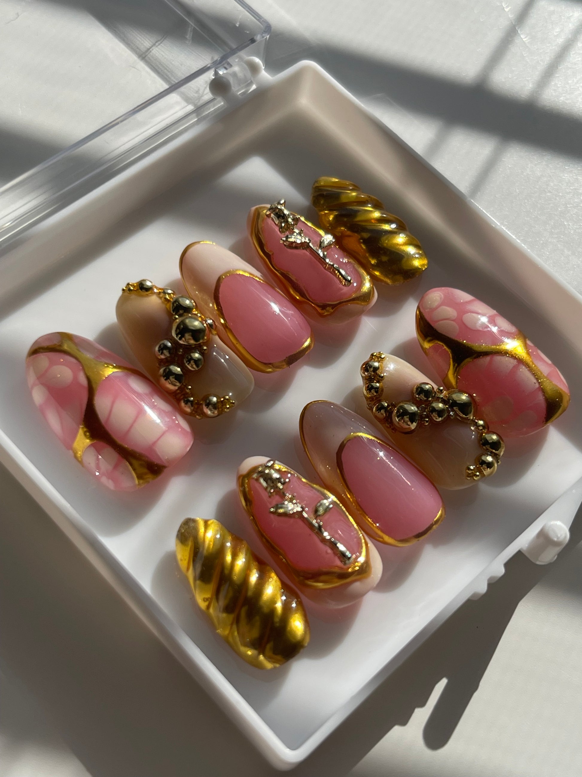 Set of pink and gold nail art designs on a white tray.