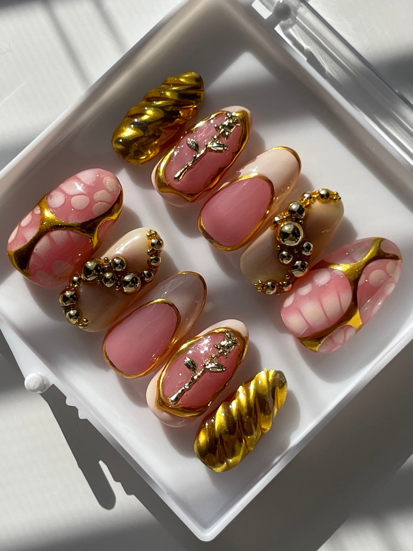 Set of pink and gold nail art designs in a white case.