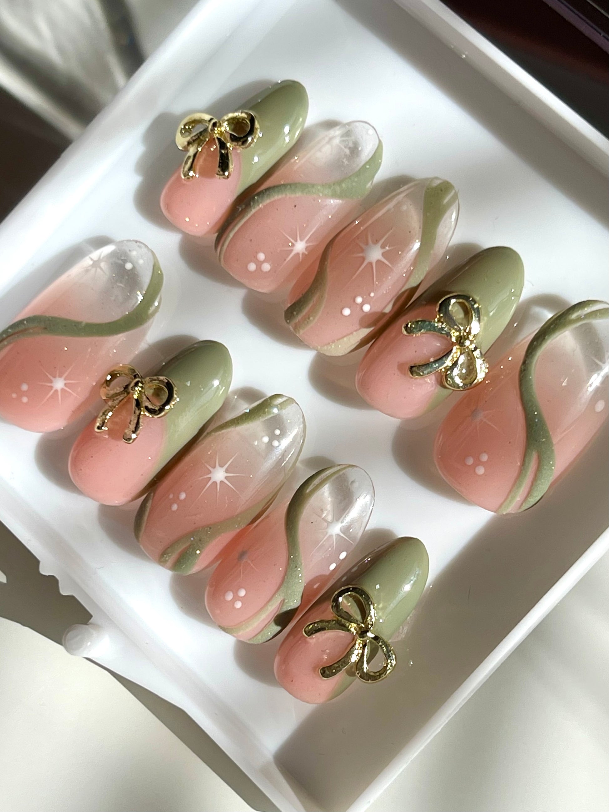 Set of decorative false nails with gold bow accents on a white tray.