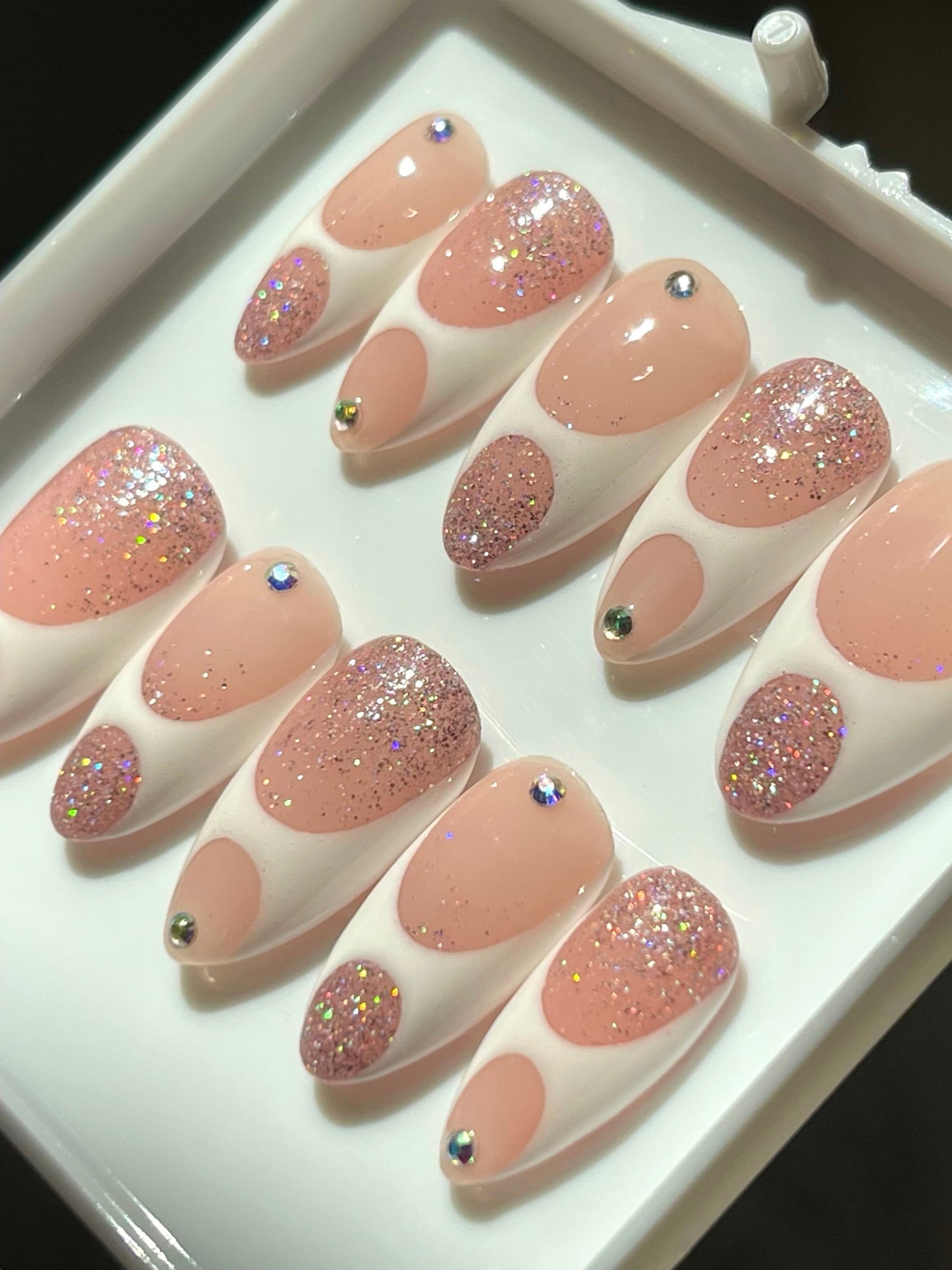 Set of pink and glittery false nails on a white tray