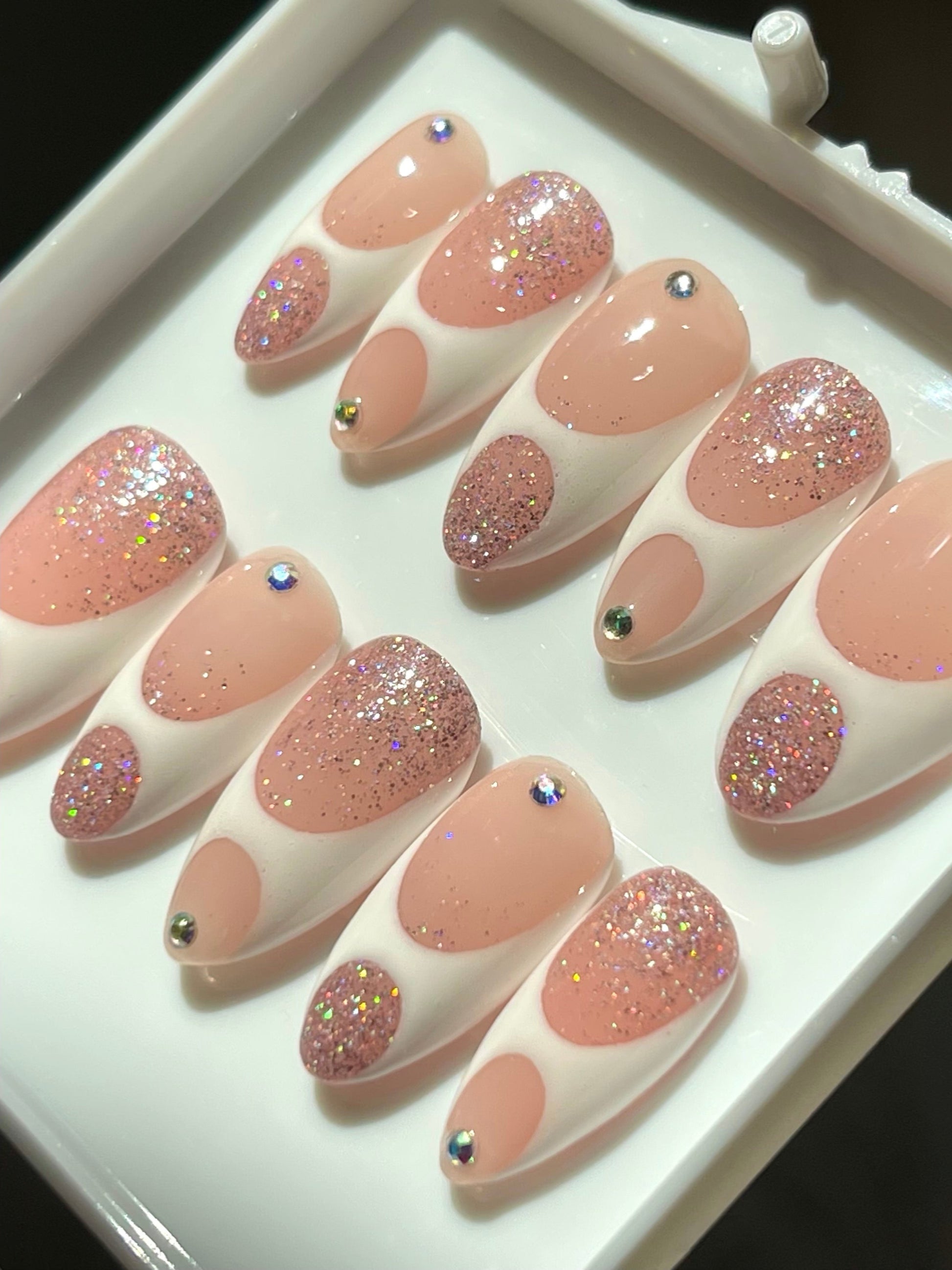 Set of pink and glittery false nails on a white tray